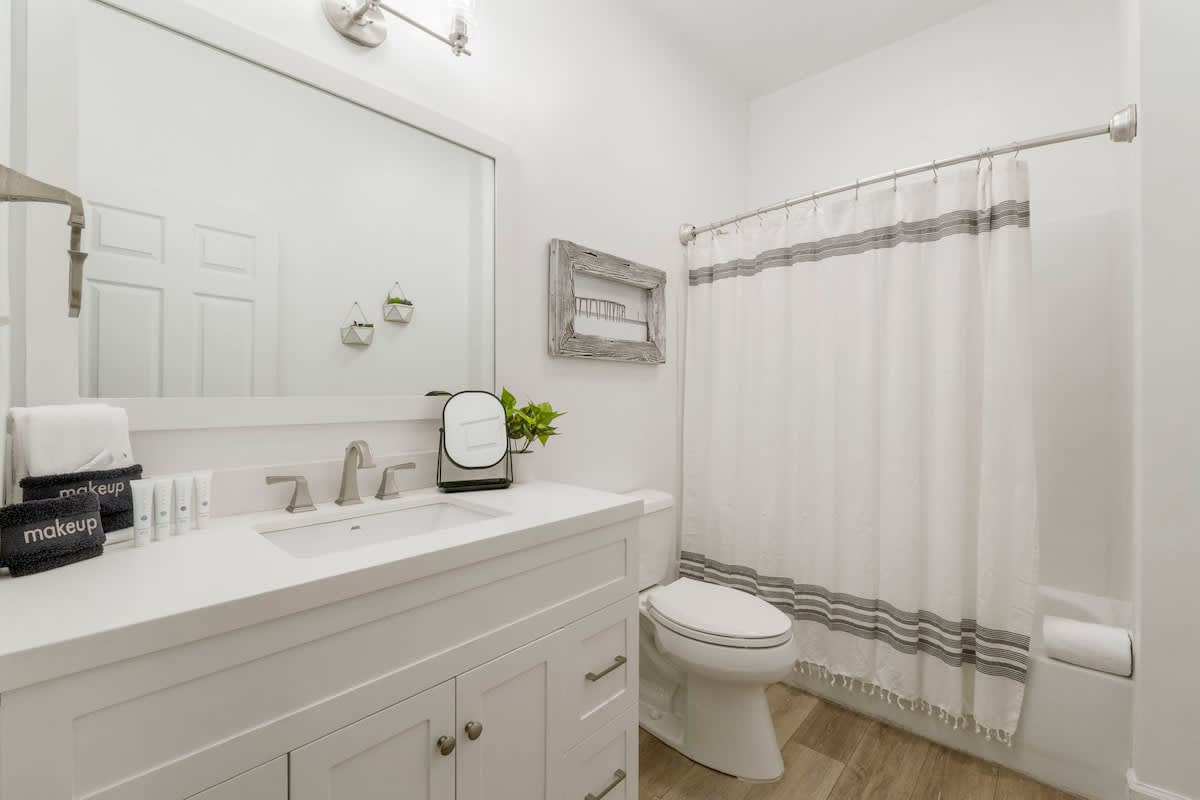 Village of SW B257 – Bright bathroom with a white vanity, large mirror, shower curtain, and wooden accents.