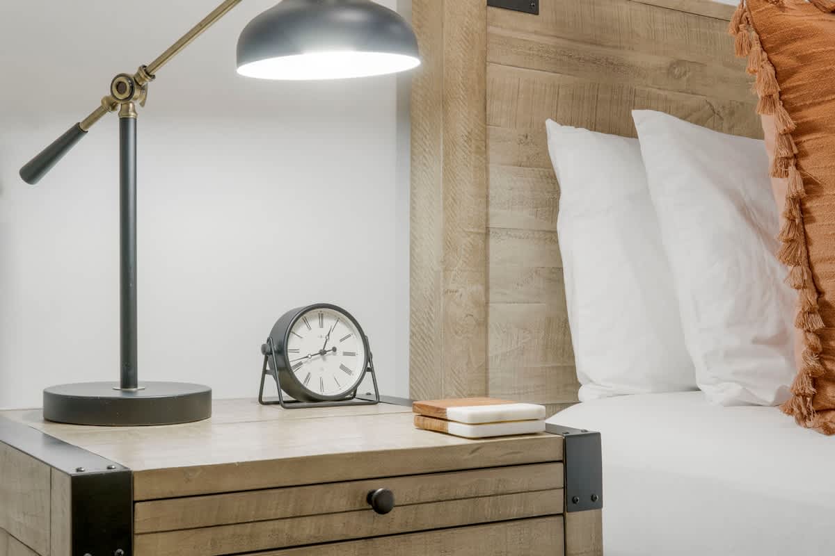 Village of SW B257 – Cozy bedroom corner with bedside table, lamp, clock, and decorative pillows.