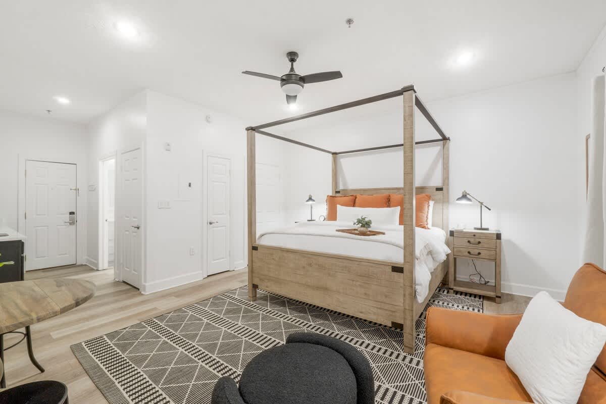 Village of SW B257 – Bedroom with a four-poster bed, decorative pillows, nightstand, chair, and patterned rug.