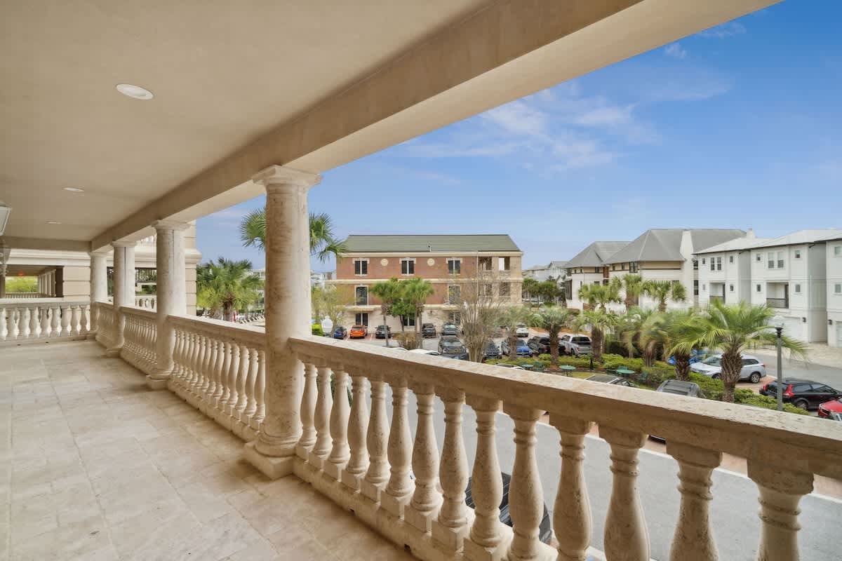 Village of SW B204 – Balcony view with decorative railing, overlooking palm trees and parked cars in a coastal neighborhood.