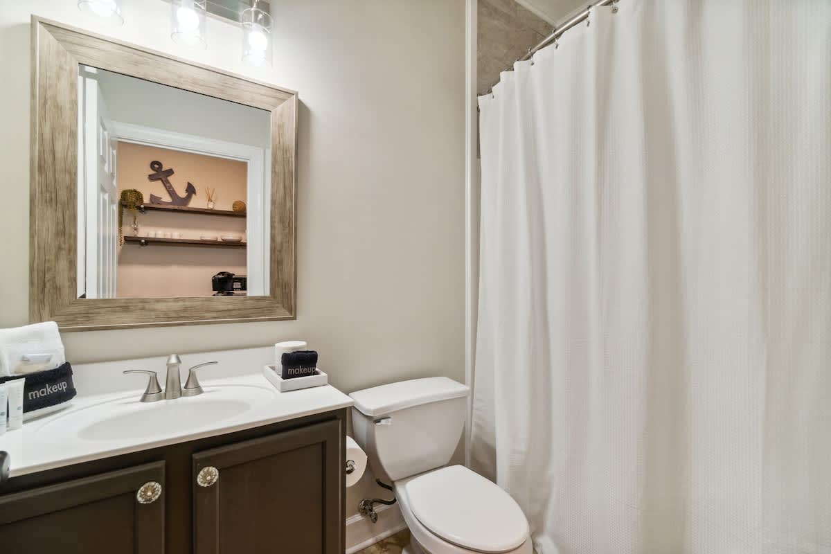 Village of SW B204 – Bathroom with a mirror, sink, toilet, and shower curtain. Neutral tones and nautical decor.