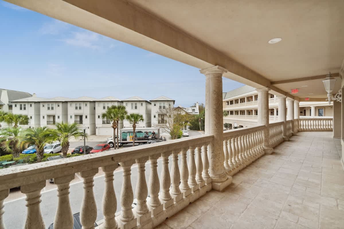 Village of SW B204 – Covered balcony with balustrade, view of nearby buildings and palm trees.