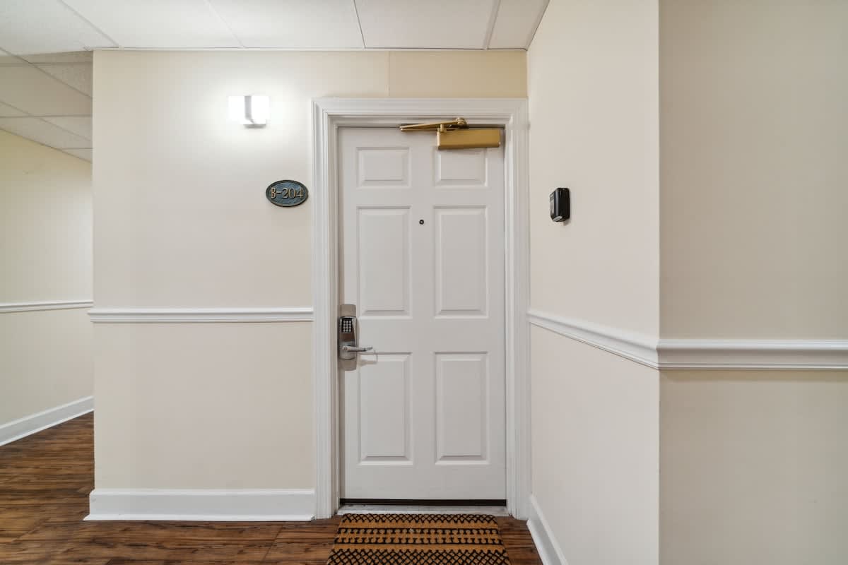 Village of SW B204 – White door with a number plate marked B204, adjacent hallway with wood flooring and wall lighting.