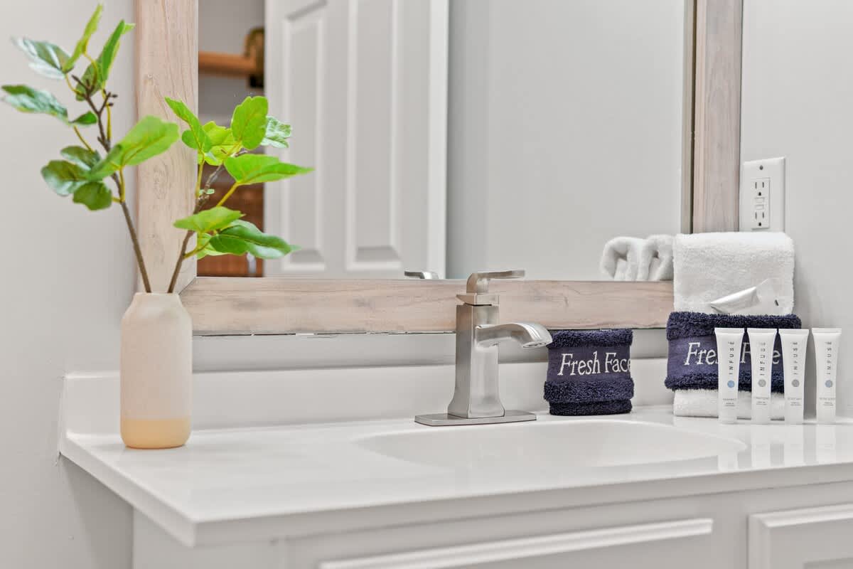 Village of SW B203 – Vanity with a modern faucet, clean white countertop, towels, and greenery in a simple vase.