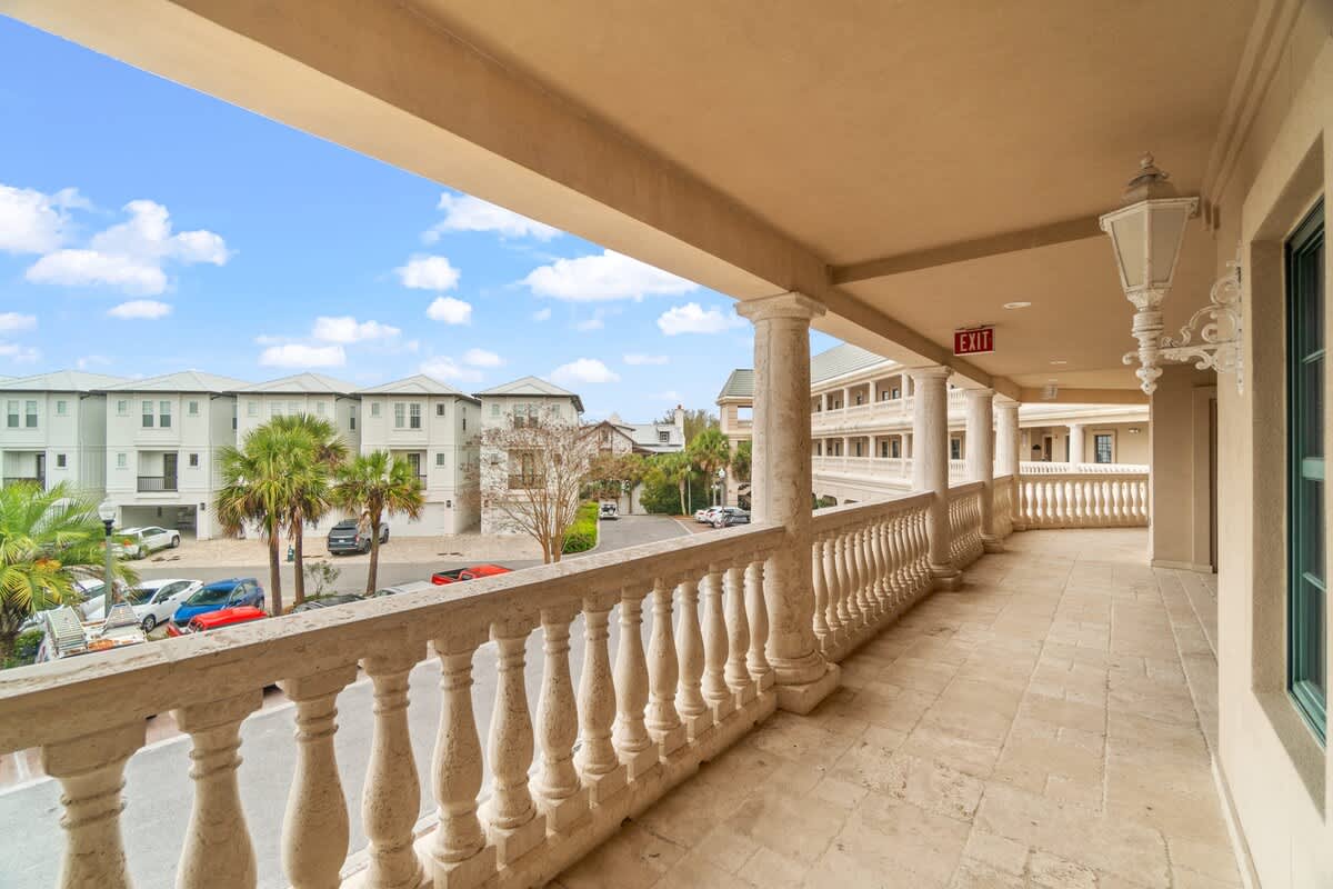 Village of SW B203 – Balcony view from rental unit with decorative railing, overlooking palm trees and parking area.