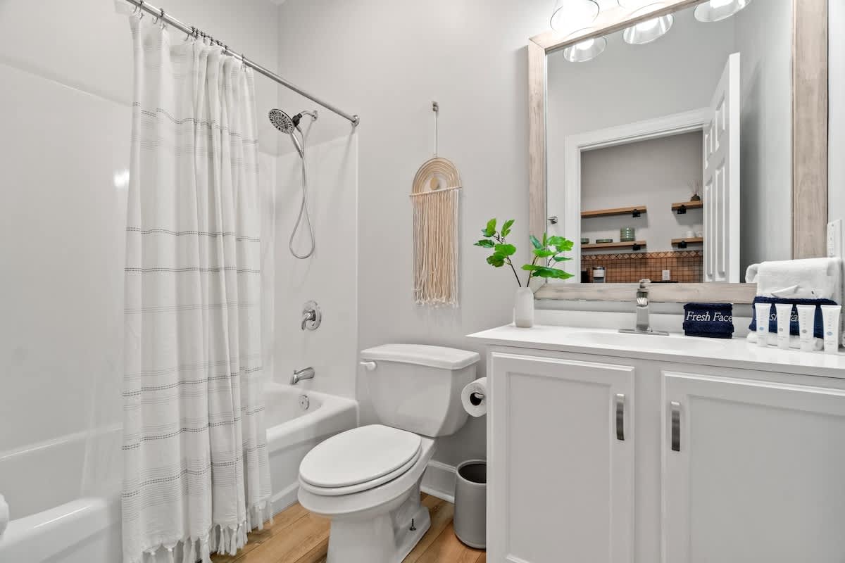 Village of SW B203 – Bathroom with a bathtub, shower curtain, vanity, mirror, and shelving.