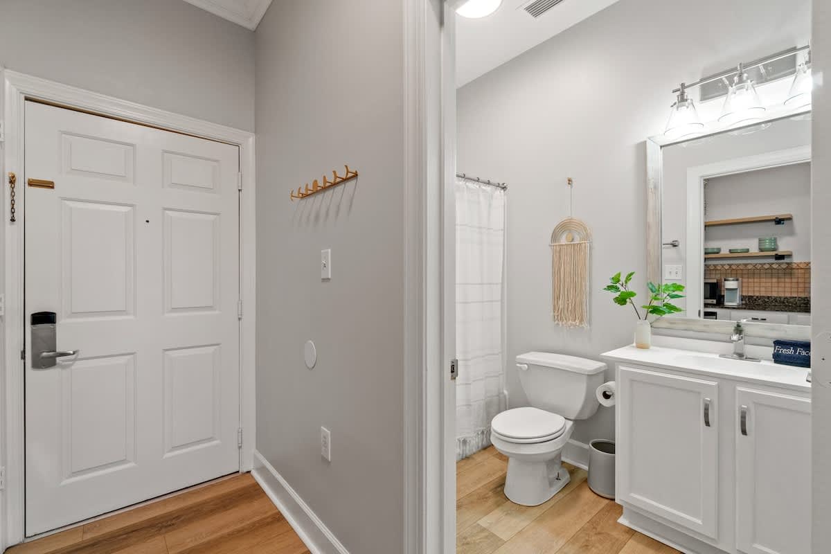 Village of SW B203 – Entryway leading to bathroom with toilet, sink, large mirror, and decorative plants.