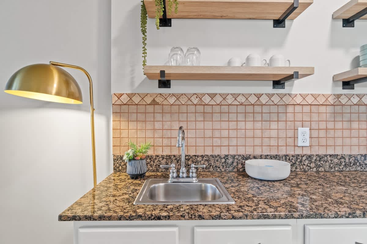 Village of SW B203 – Kitchen area with granite countertops, a sink, floating shelves, and a floor lamp.
