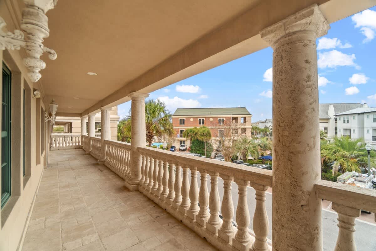 Village of SW B203 – Covered balcony with stone railing, overlooking palm trees and a nearby building.