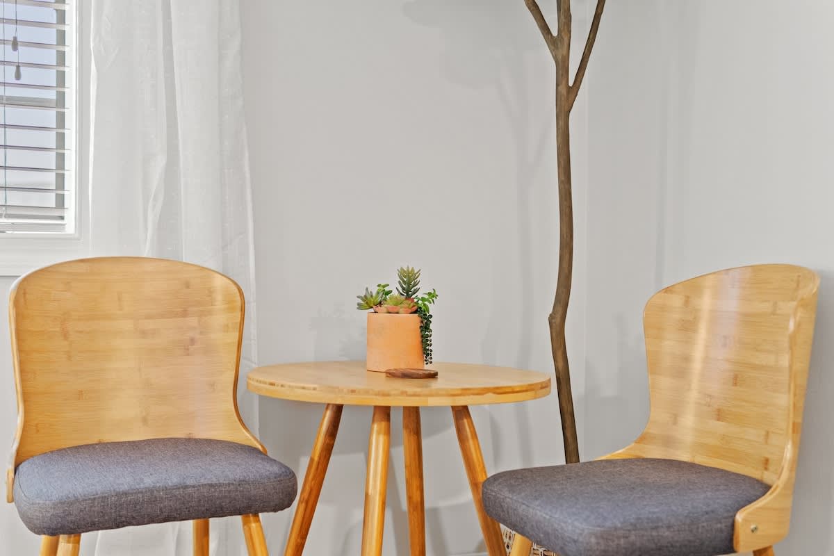 Village of SW B203 – Bamboo table and two chairs with a potted plant against a light wall.