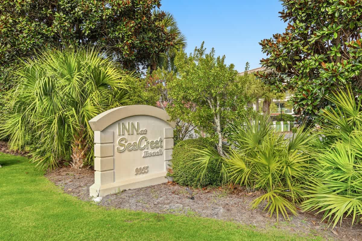 Inn at Seacrest 409 – Sign for Inn at Seacrest Beach surrounded by tropical plants and green grass.