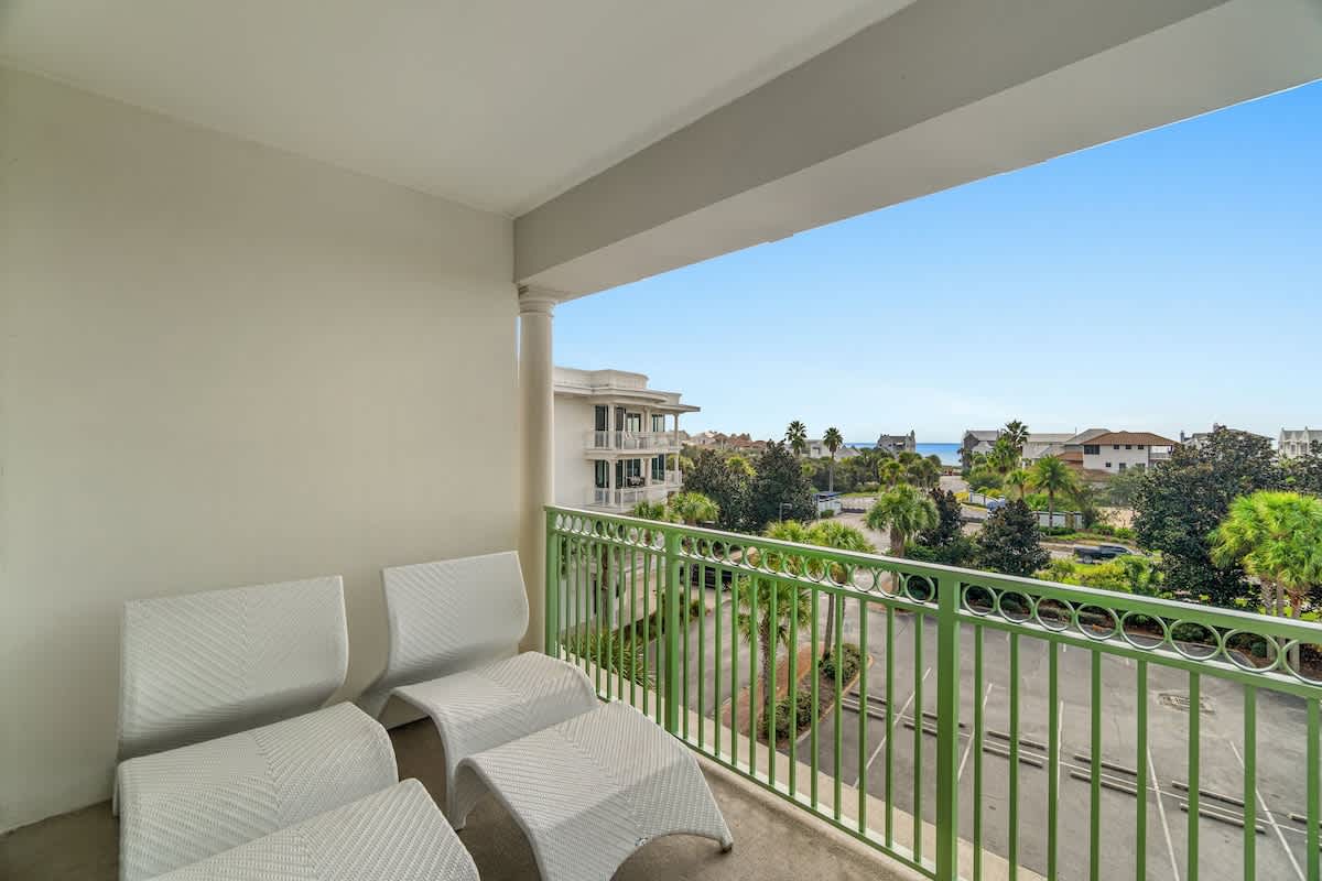Inn at Seacrest 409 – Balcony with white lounge chairs and a view of palm trees and the ocean.