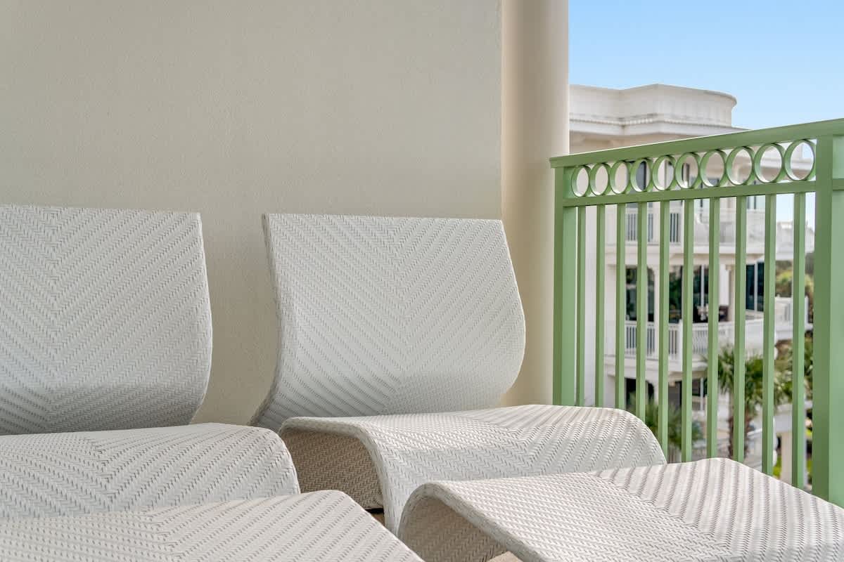 Inn at Seacrest 409 – White lounge chairs on a balcony with green railing, overlooking a palm tree view and light blue sky.