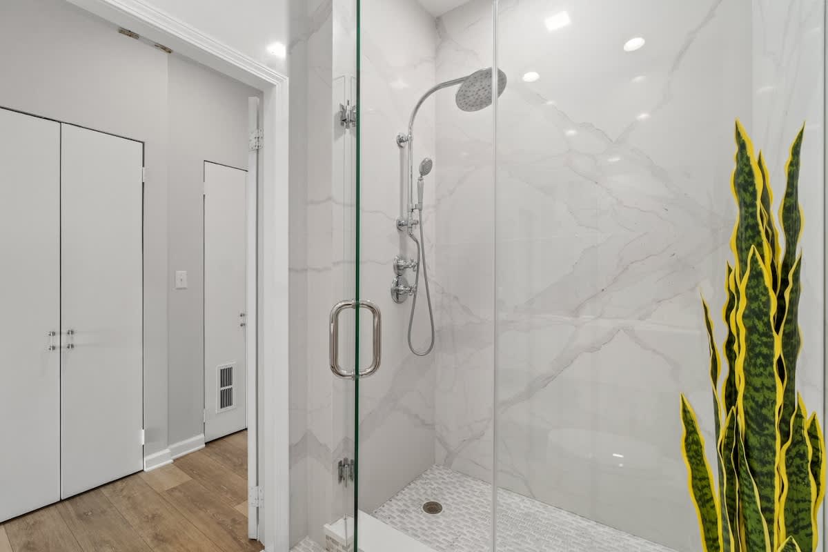Inn at Seacrest 409 – Modern shower with glass doors, marble walls, and plant accent in a bathroom setting.