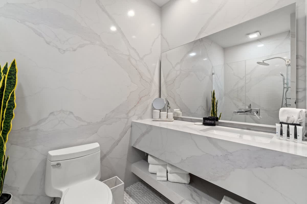 Inn at Seacrest 409 – Modern bathroom with marble walls, a toilet, sink, mirror, and decorative plants.