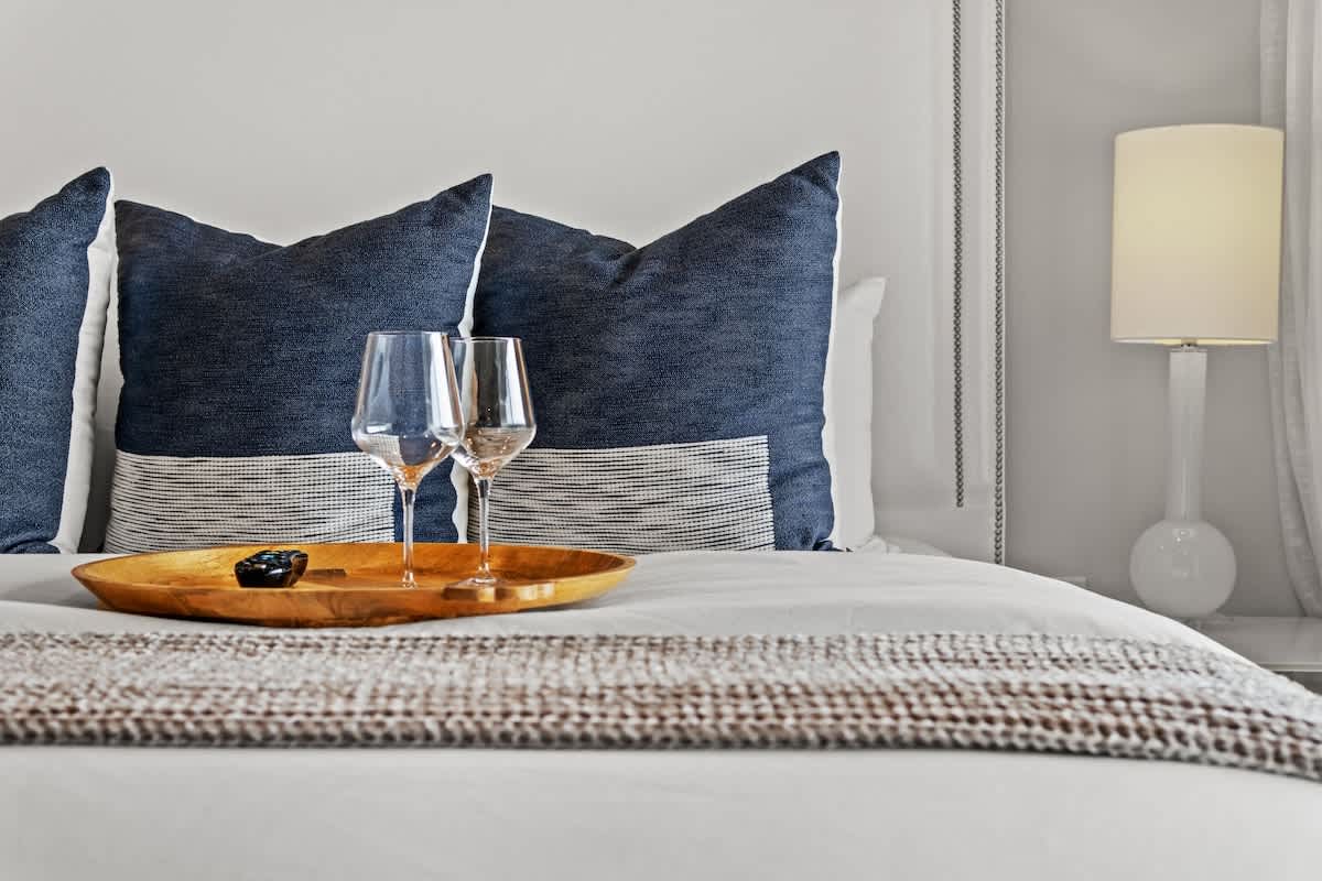 Inn at Seacrest 409 – Two wine glasses on a wooden tray with decorative pillows in a well-lit bedroom.