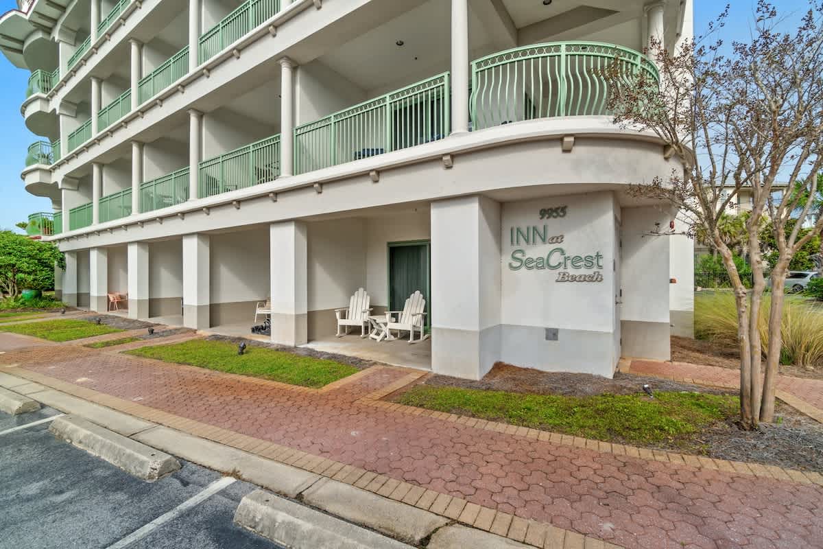 Inn at Seacrest 409 – Exterior of the Inn at Seacrest 409 showing white building, green balconies, and patio chairs.