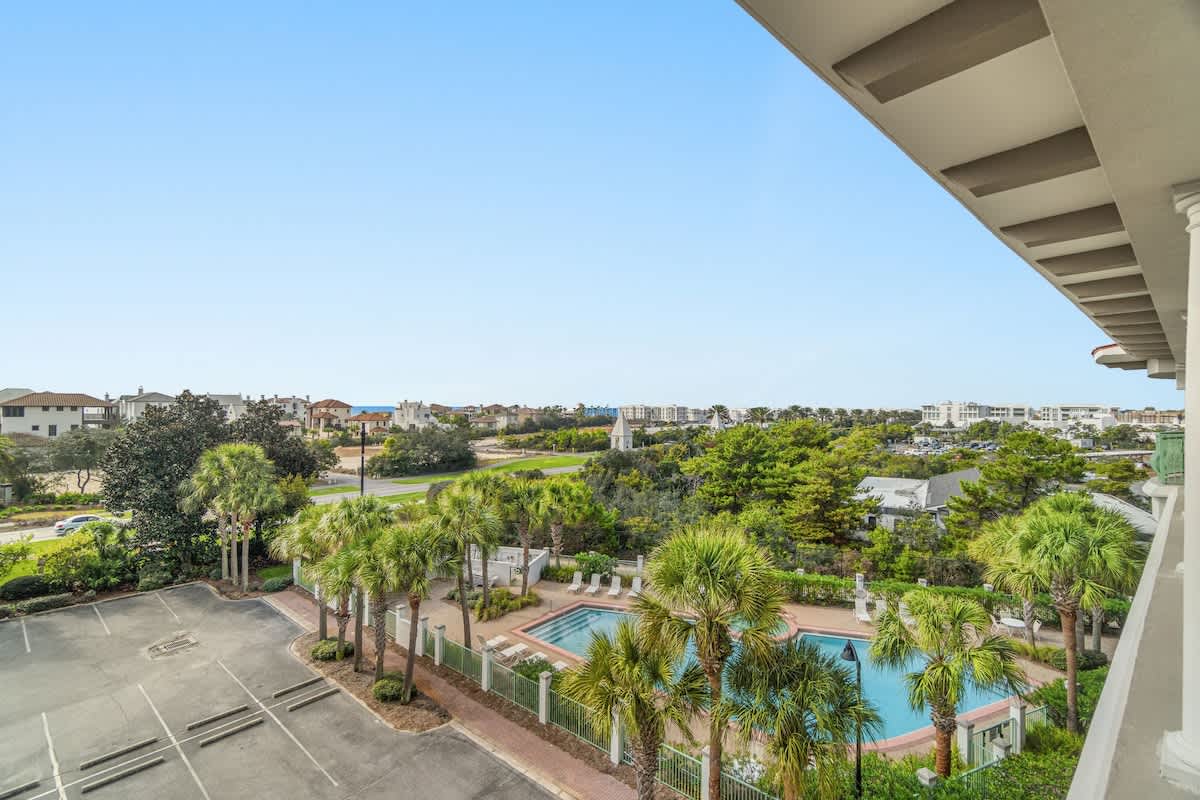 Inn at Seacrest 409 – View from balcony showing a pool, palm trees, parking lot, and distant beach houses.