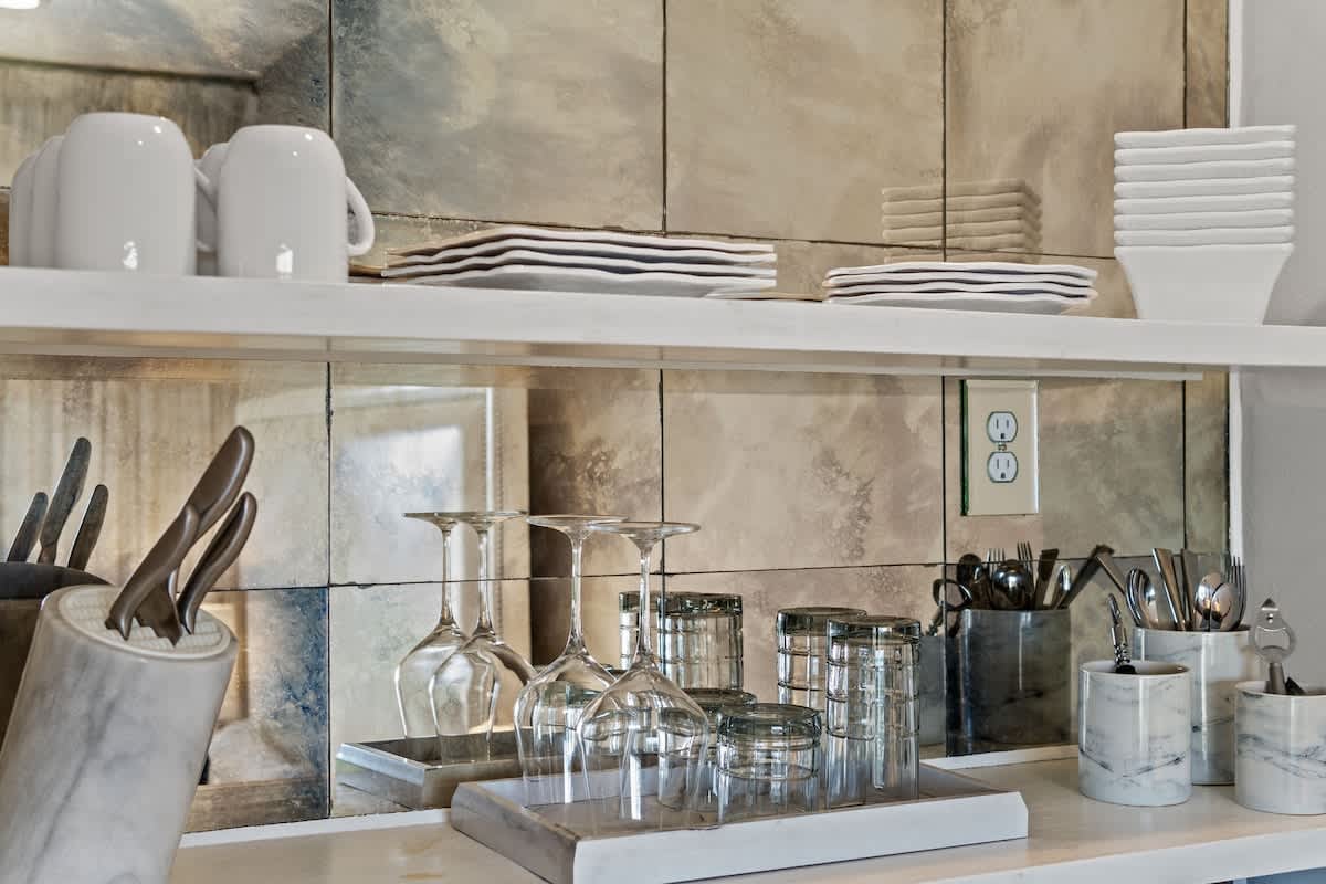 Inn at Seacrest 409 – Modern kitchenette with white mugs, plates, glasses, utensils, and marble accents against mirrored backsplash.