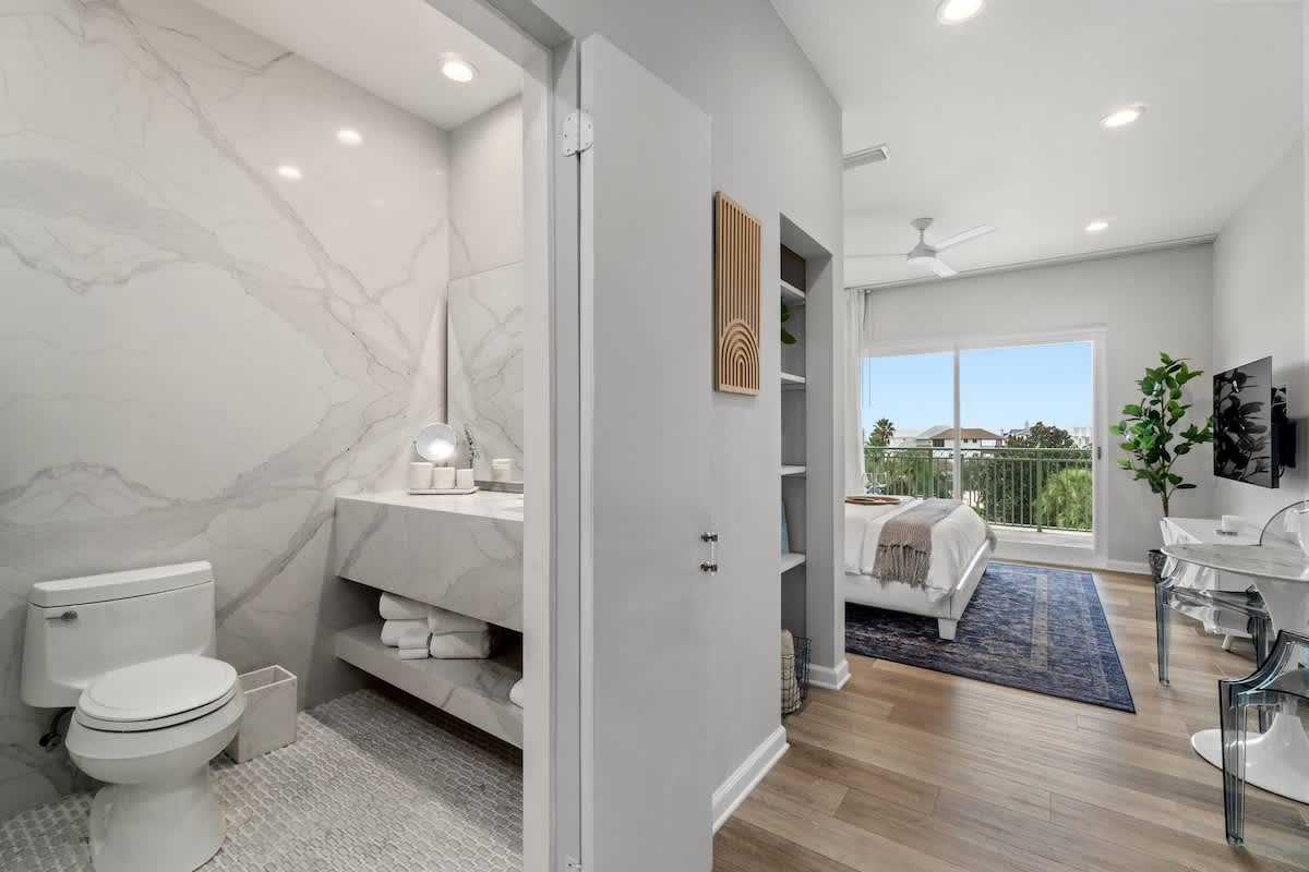 Inn at Seacrest 409 – Bathroom with marble walls, bedroom with large windows, and view of greenery.