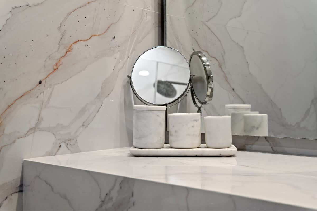 Inn at Seacrest 409 – Marble bathroom countertop with round mirror and white cylindrical containers.