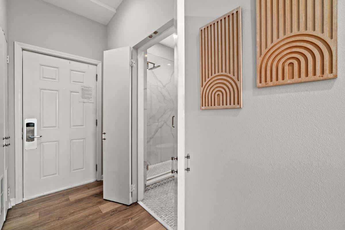 Inn at Seacrest 409 – Entryway with wooden floor, decorative wall art, open doors leading to bathroom with glass shower.
