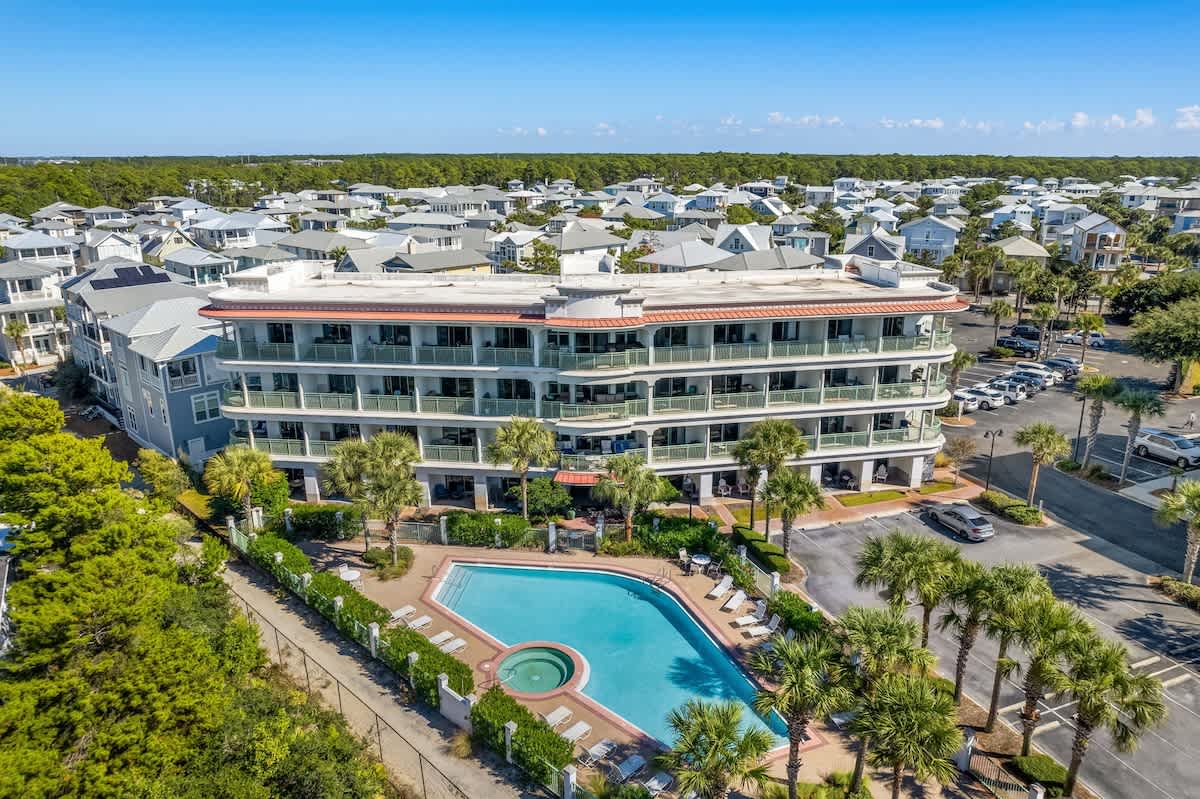 Inn at Seacrest 409 – Aerial view of a three-story building with balconies, a pool, and surrounding palm trees.