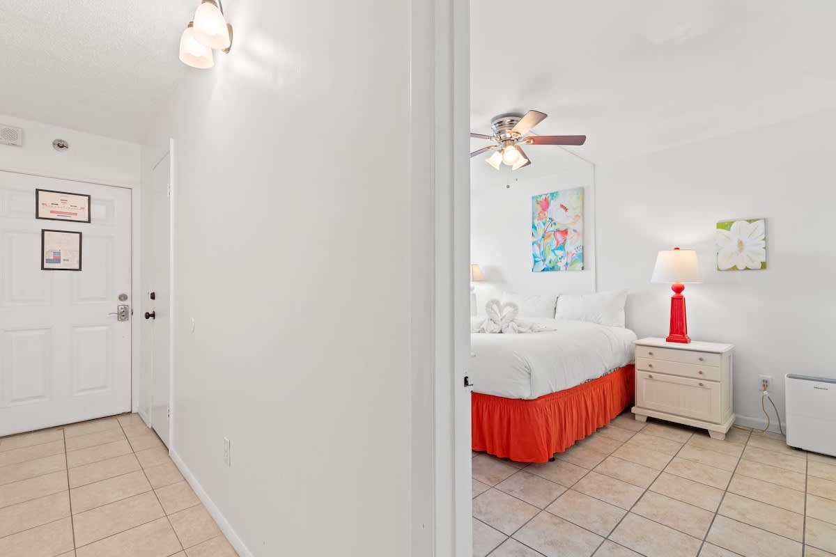 The Summit 1009 – Interior view of a bright bedroom featuring a king bed, artwork, and a lamp with a dresser.