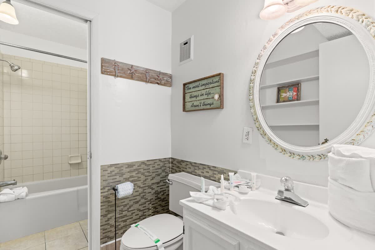 The Summit 1009 – Bright bathroom featuring a shower/tub combo, white sink, decorative mirror, and tiled accents.