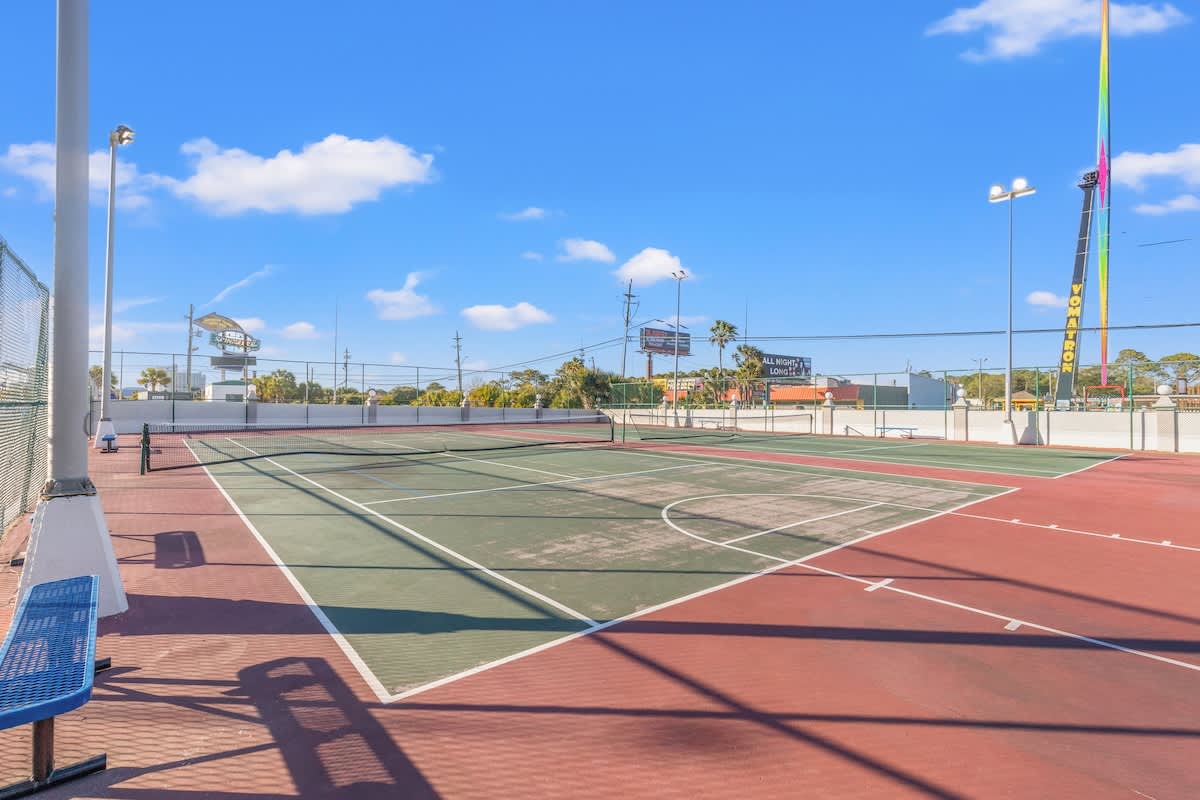 The Summit 1009 – Tennis court with net, surrounded by palm trees and buildings under a blue sky.
