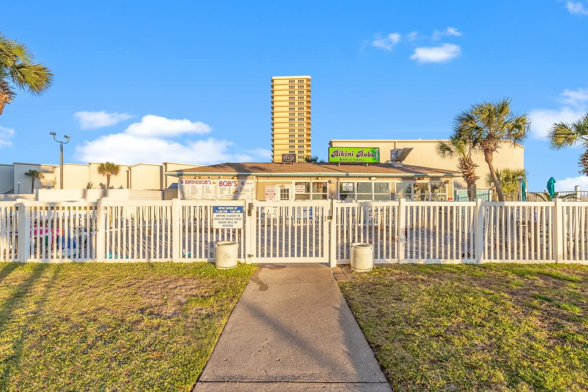 The Summit 1009 – Outdoor view of Bikini Bob's Bar & Grill with palm trees and a pathway leading to the entrance.