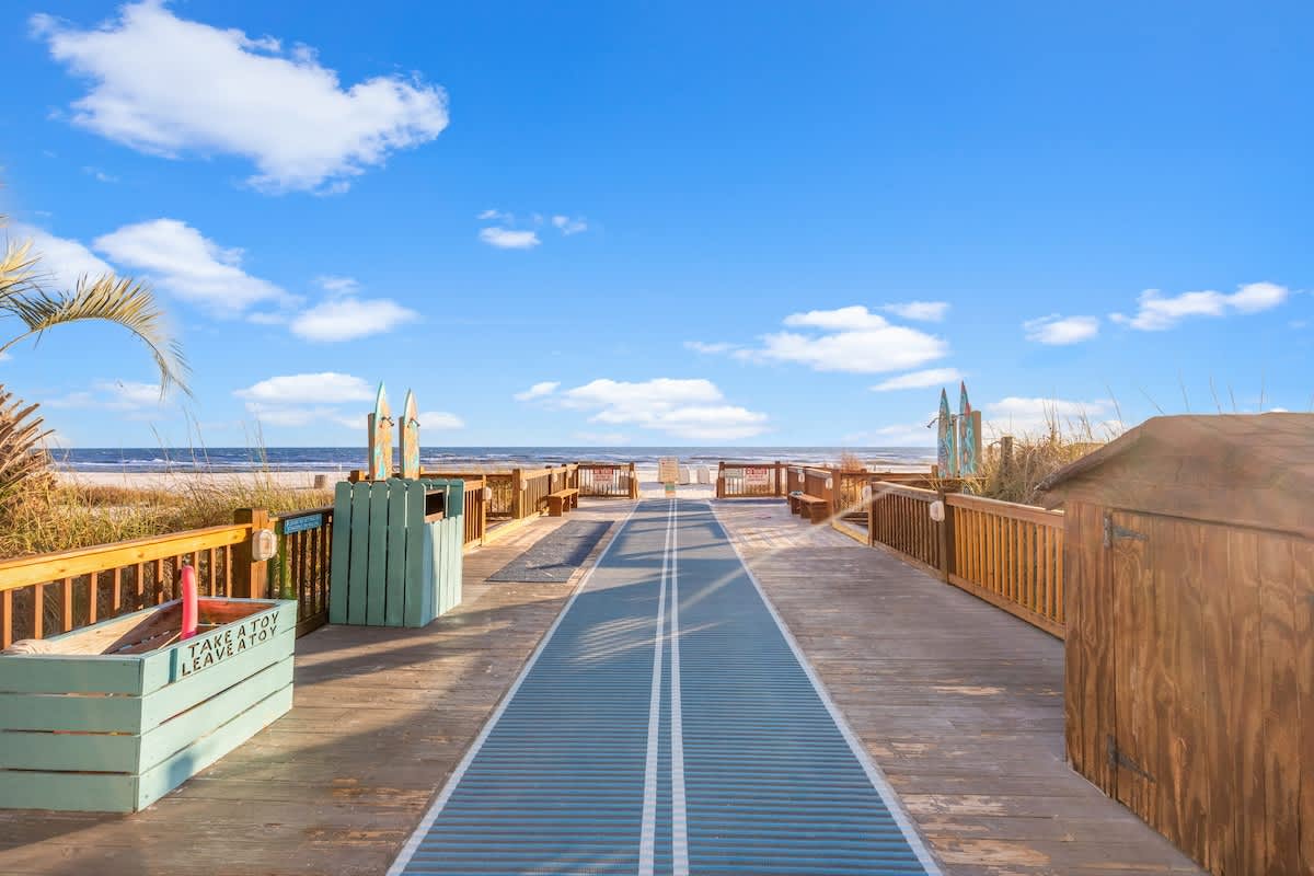 The Summit 1009 – Wooden boardwalk leading to the beach with blue skies and palm plants on either side.