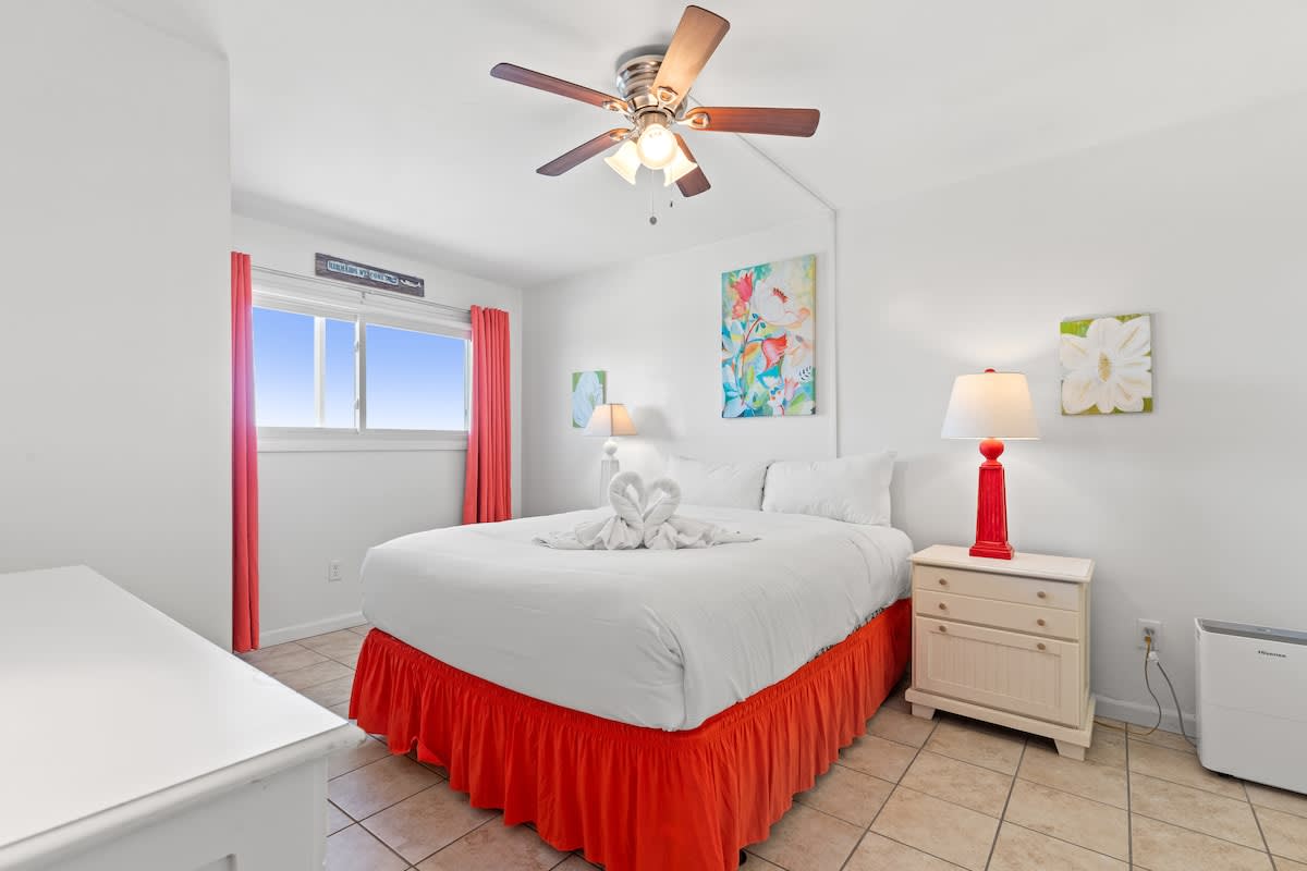 The Summit 1009 – Bright bedroom with a queen bed, ceiling fan, art, side tables, and window curtains.