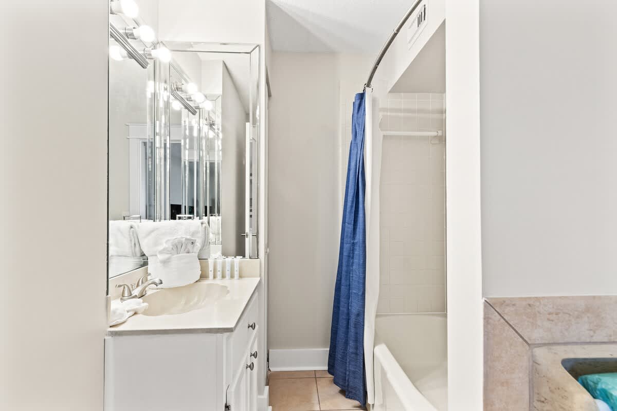 The Summit 301 – Bathroom with sink, mirror, shower curtain, and toiletries on countertop.