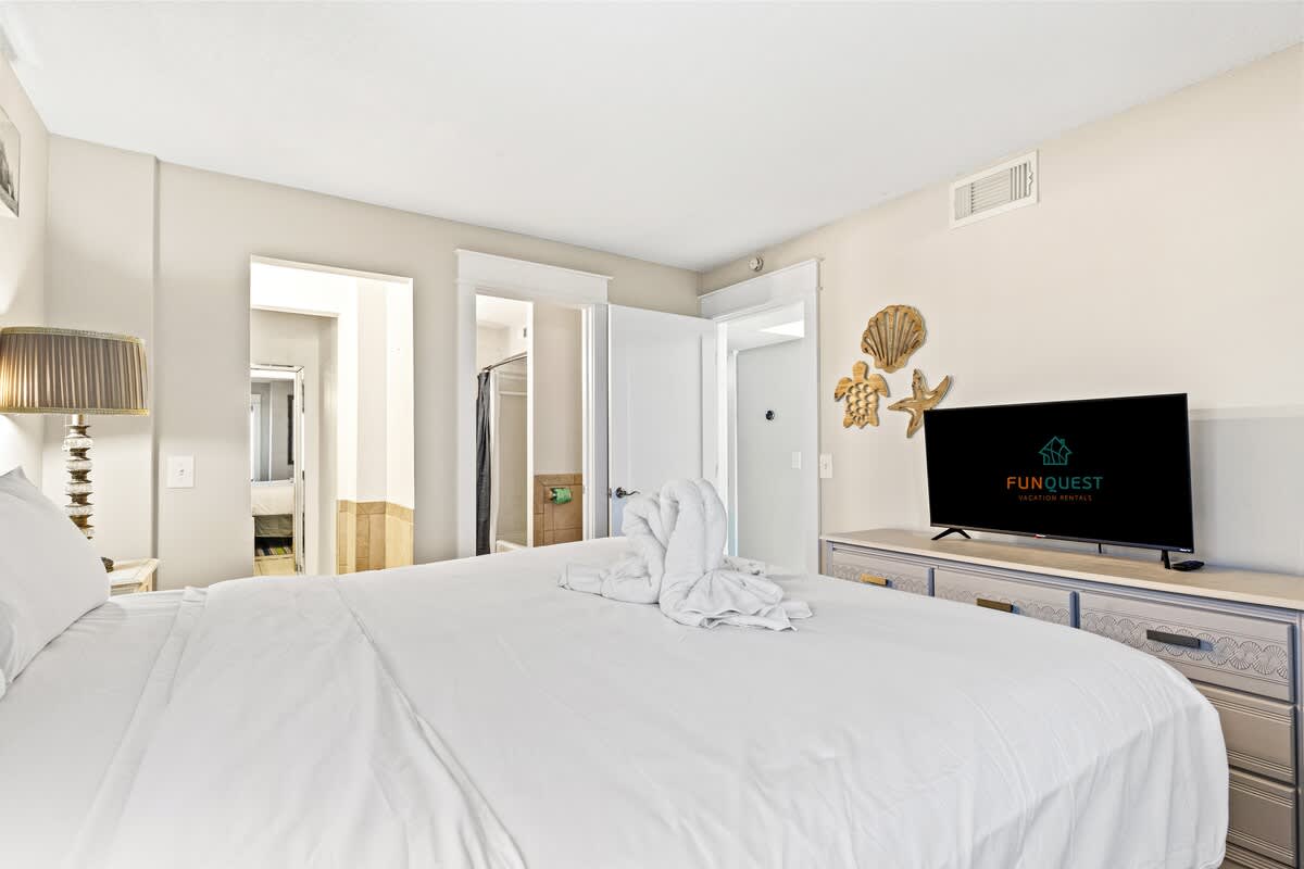 The Summit 301 – Bedroom with a large bed, lamp, TV, and bathroom access.