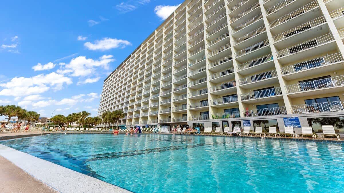 The Summit 229  – Exterior view of a tall hotel building beside a swimming pool with palm trees and blue sky.
