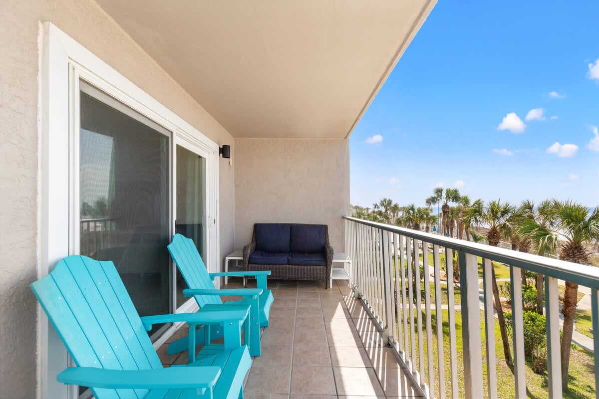 The Summit 301 – Balcony with turquoise chairs, a sofa, and views of palm trees and blue sky.