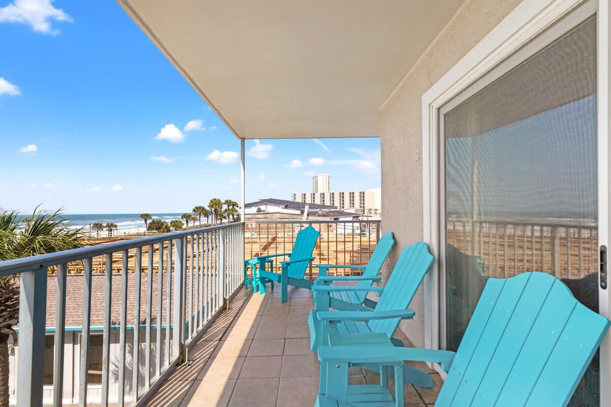 The Summit 301 – Balcony with blue Adirondack chairs overlooking the ocean and palm trees.