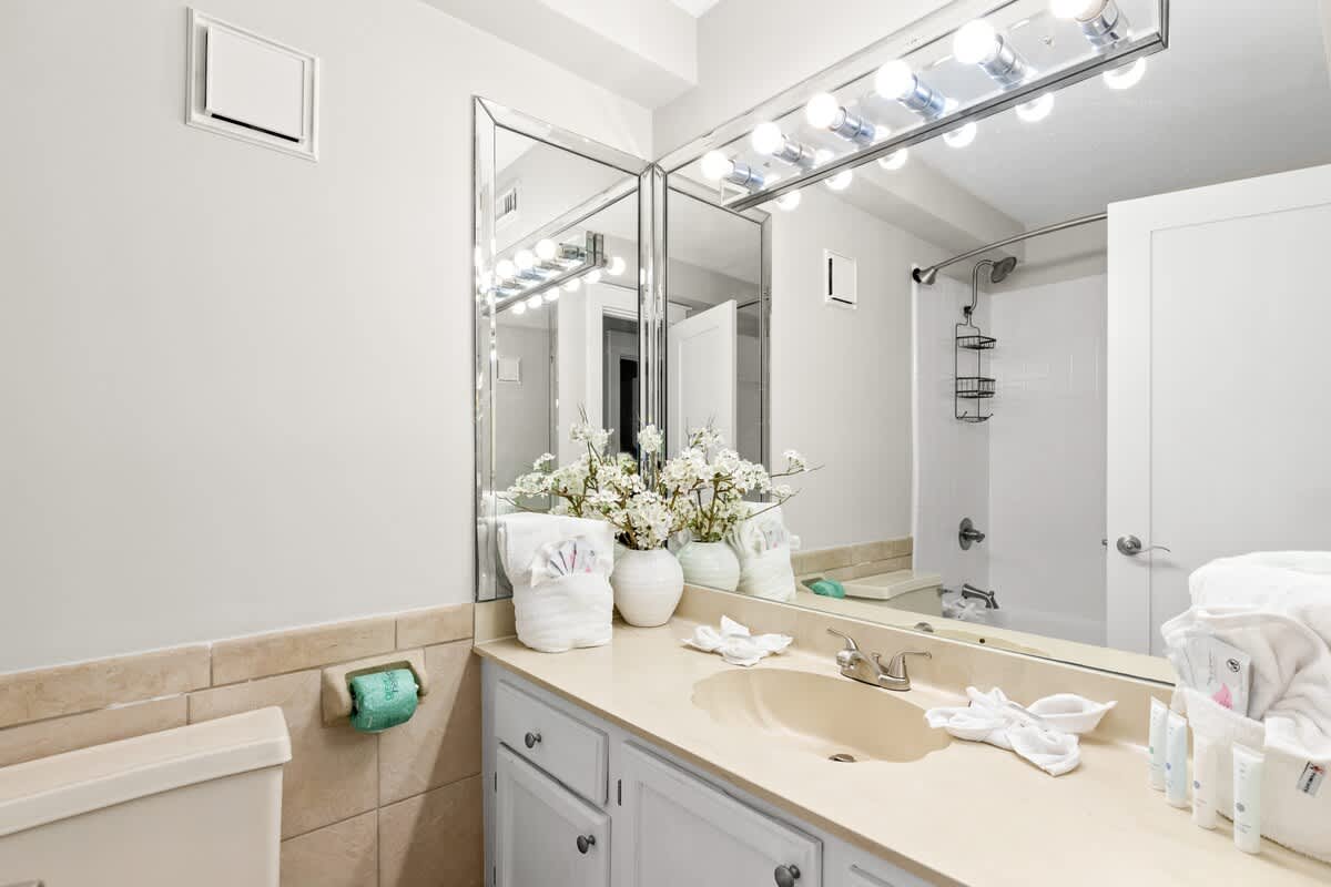 The Summit 301 – Bright bathroom with double mirrors, beige countertop, decorative flowers, and shower area visible.