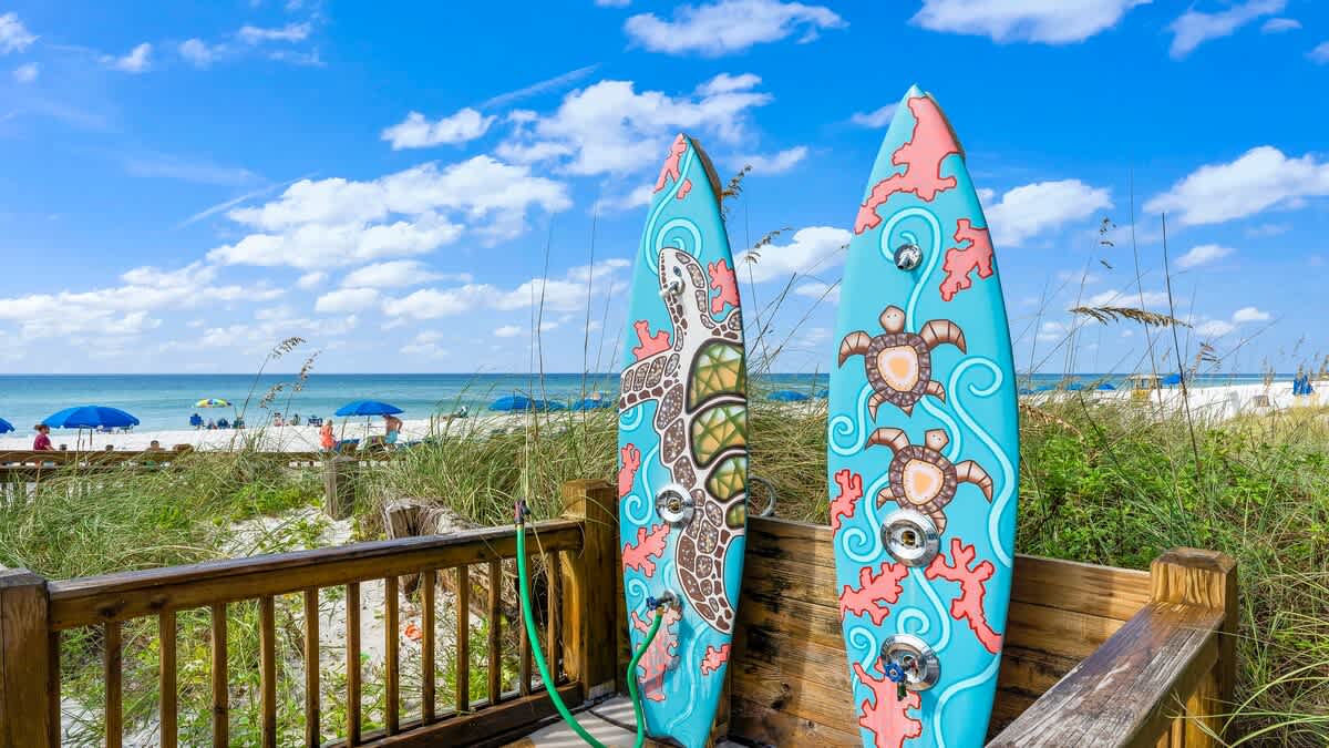 The Summit 229  – Two decorative surfboards on a wooden deck overlooking a sandy beach with umbrellas and ocean in the background.
