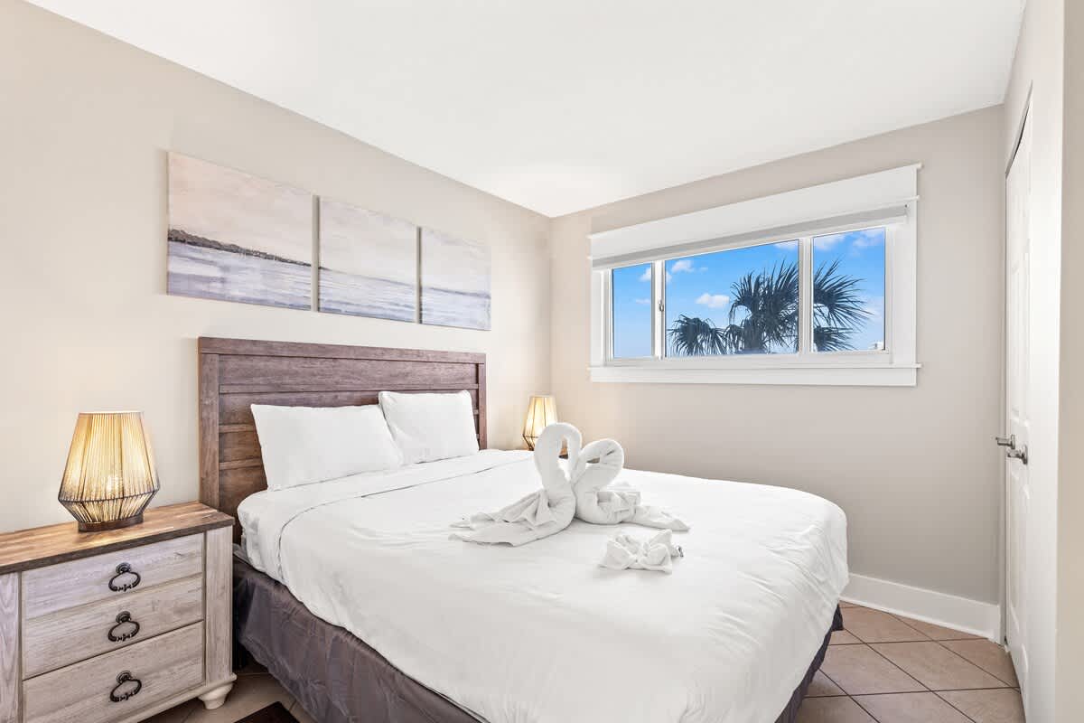The Summit 301 – Cozy bedroom with queen bed, decorative towels, and window view of palm trees and blue sky.