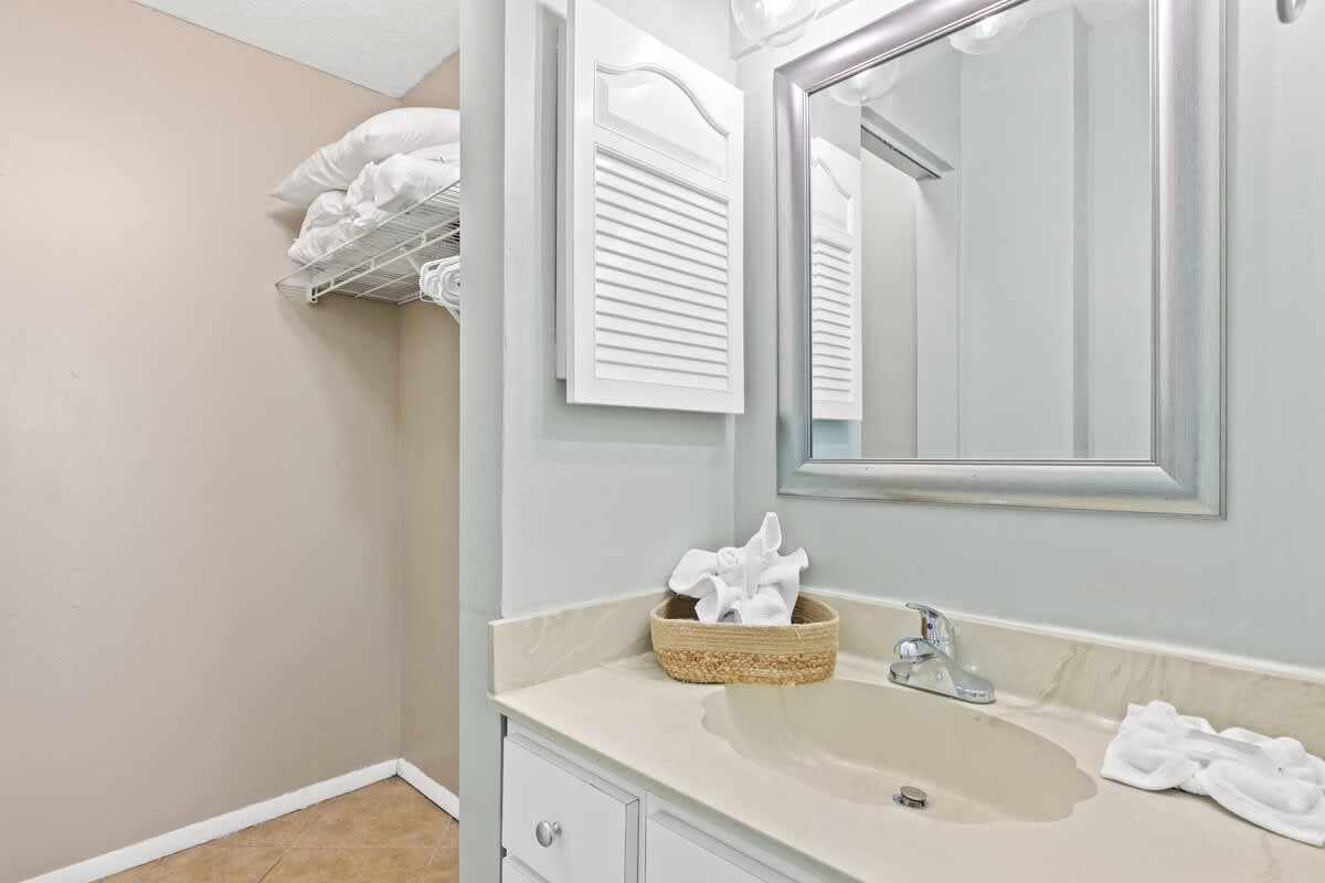 The Summit 632 – Bathroom with beige walls, sink, mirror, and shelf storing white linens.
