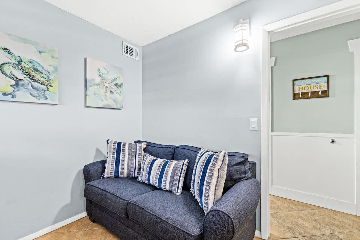 The Summit 632 – Cozy seating area with a blue sofa and decorative pillows, artwork on walls, and entryway to another room.