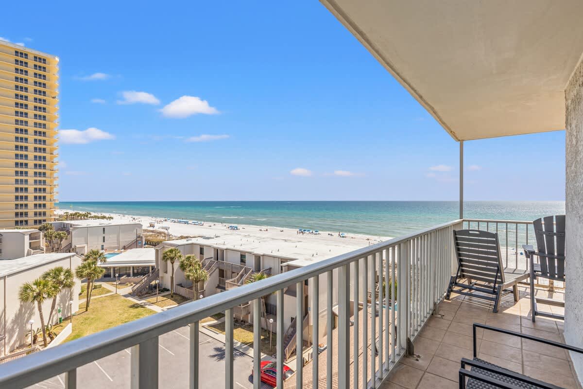 The Summit 632 – Balcony view of beach, ocean, and coastal buildings with two chairs overlooking the water.