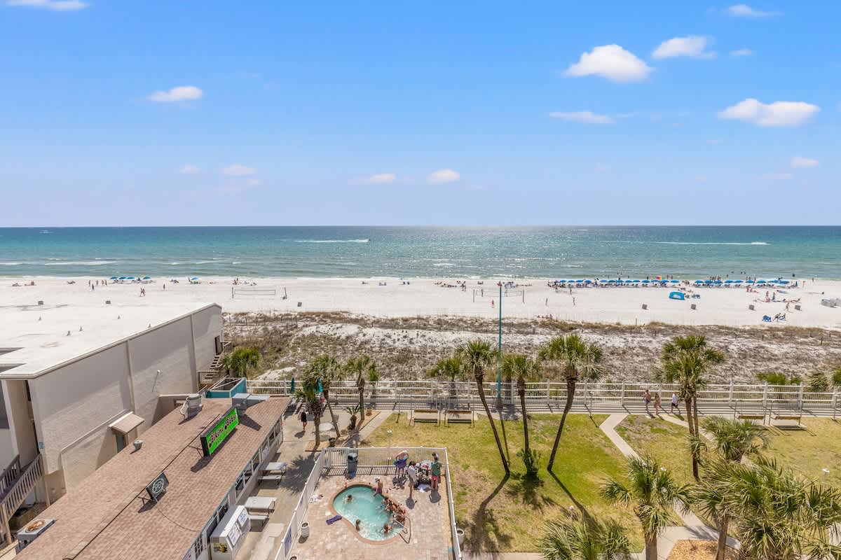 The Summit 632 – Oceanfront view from a balcony, showing beach, palm trees, pool area, and people enjoying the sun.
