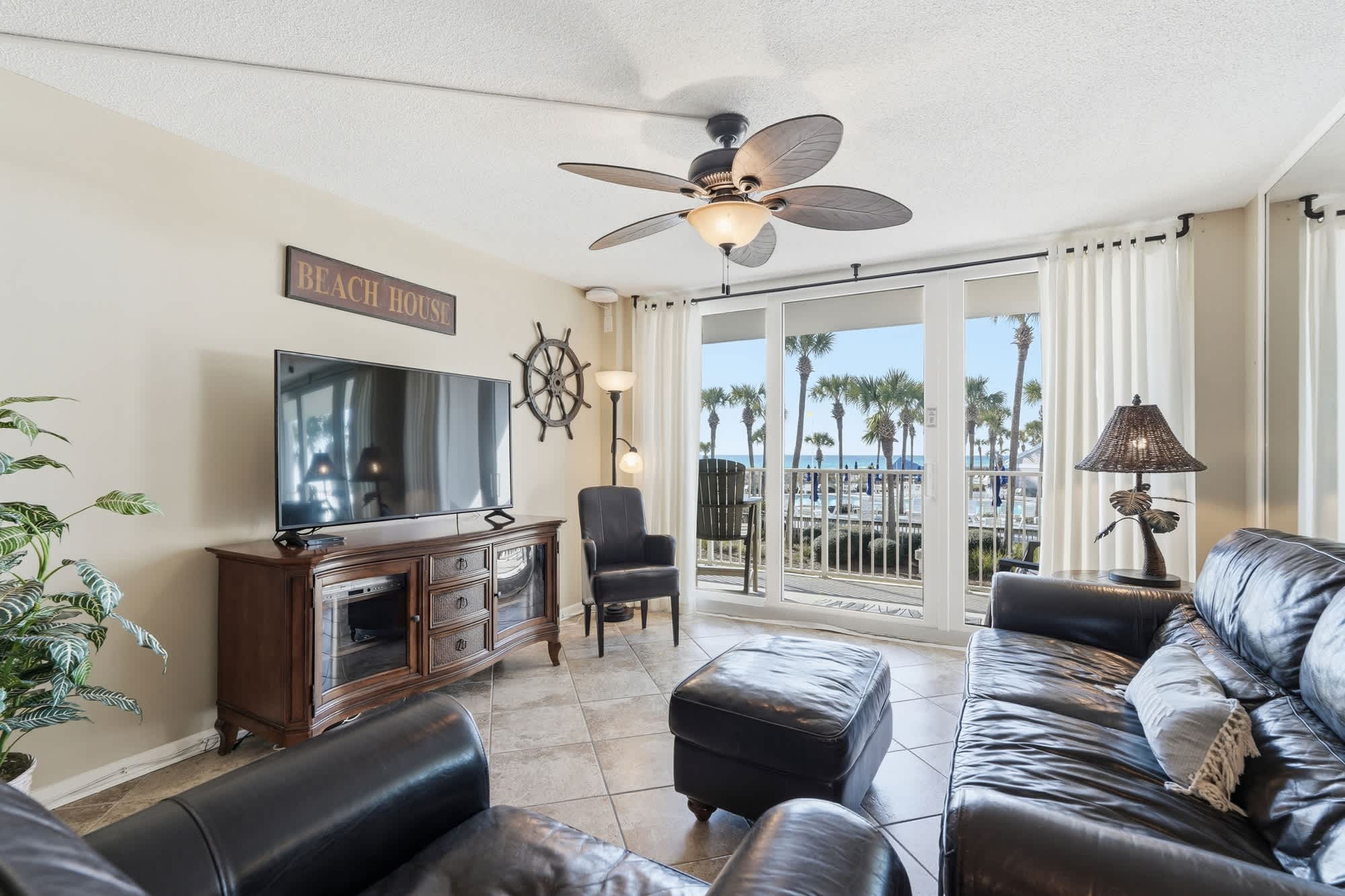 Dunes C104 – Cozy living room with leather furniture, TV, and palm tree view through sliding glass doors.