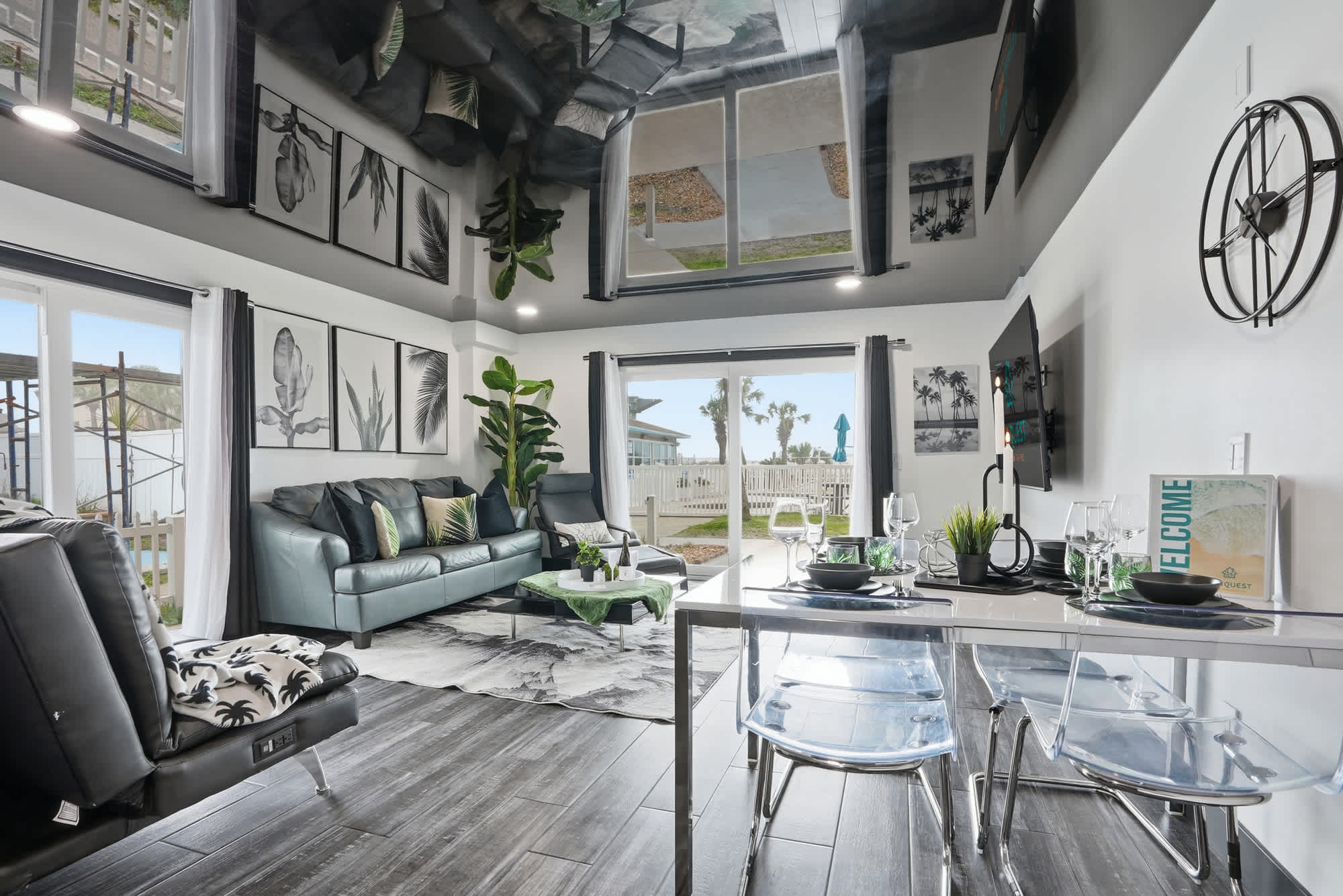 The Summit 132 – Living room with modern furniture, dining area, large windows, and a view of outdoor space and palm trees.