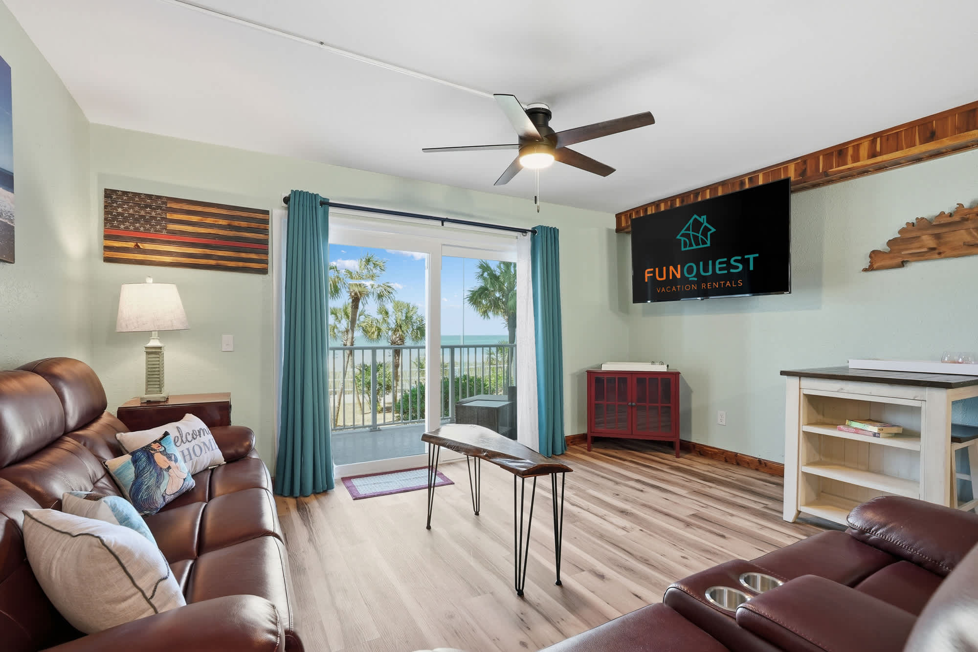 The Summit 206 – Living room with leather sofas, fan, wall-mounted TV, and a balcony view of palm trees and the ocean.