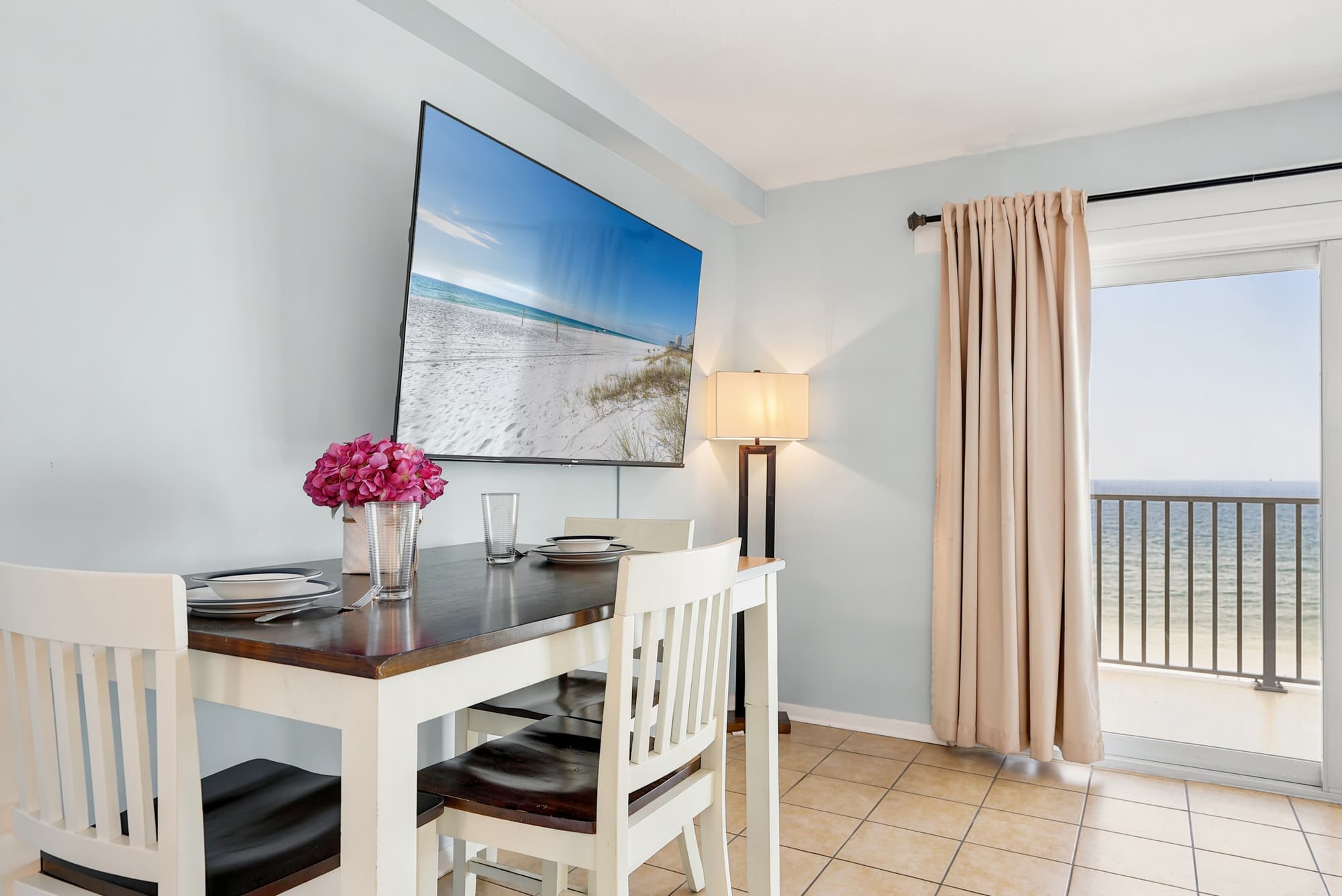 The Summit 1021 – Dining area with table, chairs, large TV, and ocean view through glass door.