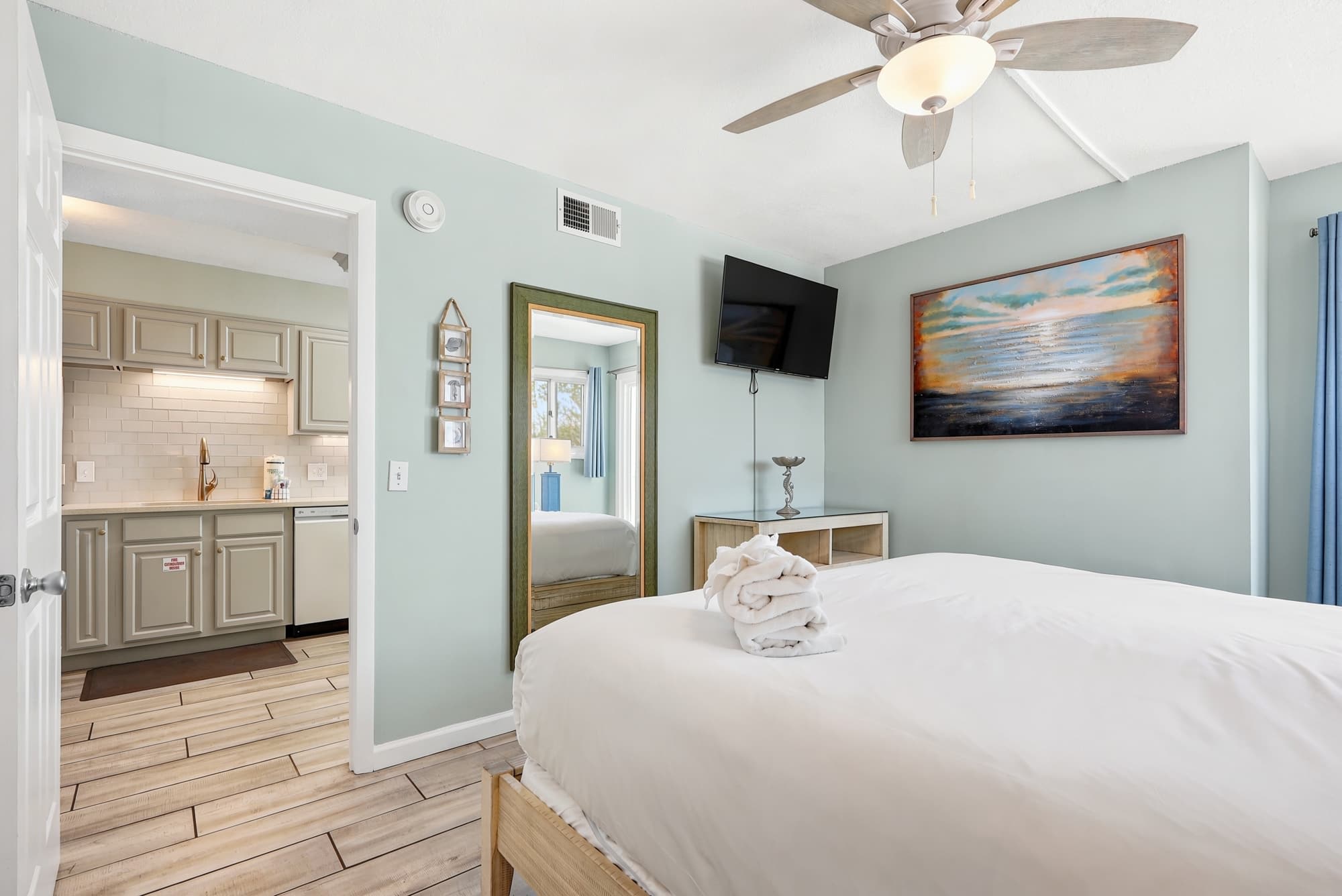 The Summit 1101 – Bedroom with a king-sized bed, kitchenette, TV, and artwork on light blue walls.
